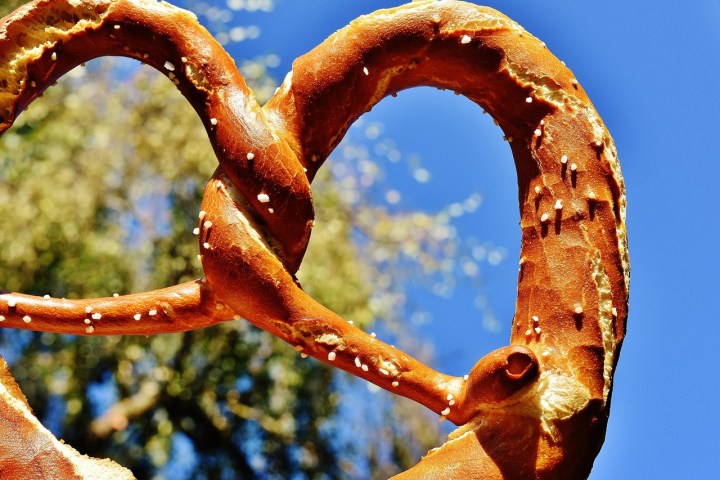 Close-up of a pretzel against a blue sky with tree branches in the background.
