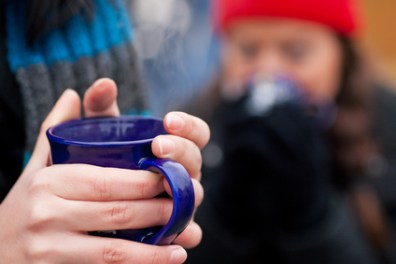 Close-up of hands holding a blue mug, blurred person in red hat in background.