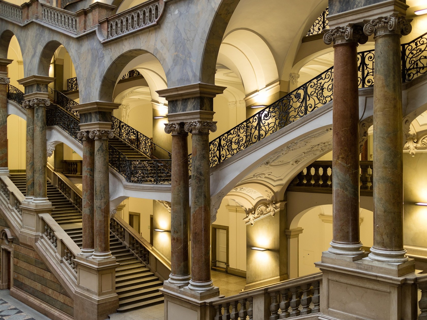 Elegant staircase with arches, ornate railings, and columns in a historic building.