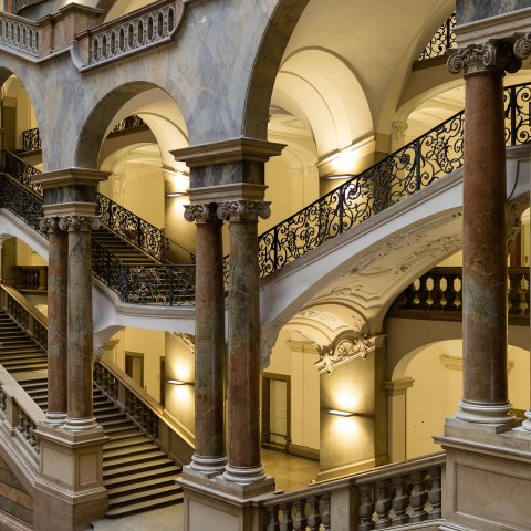 Elegant staircase with arches, ornate railings, and columns in a historic building.