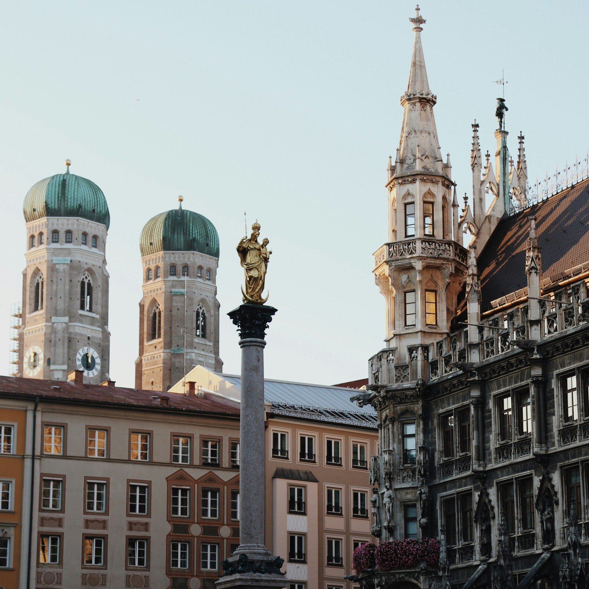 City square with historic towers, column with statue, ornate building, and clear sky.