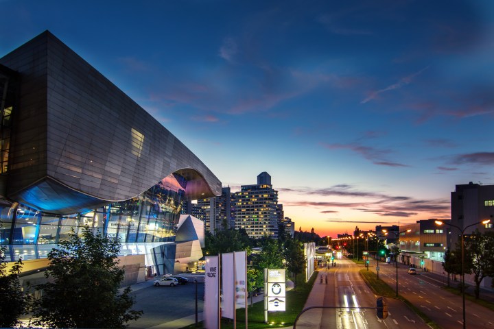 Modern building and city street at dusk with glowing lights and a colorful sky.