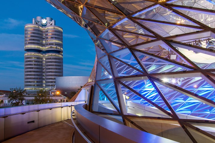 Modern building with glass facade and a cylindrical skyscraper in the background during dusk.