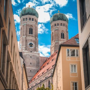 Two church towers with green domes between buildings and a blue sky.