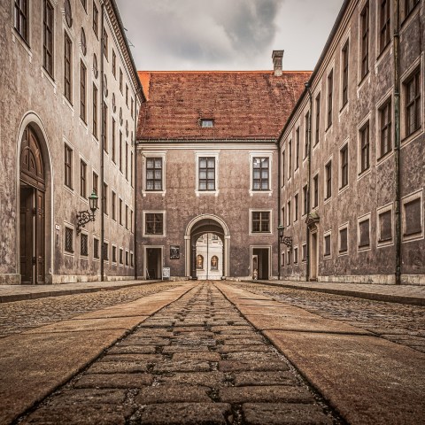 Low-angle view of a cobblestone alley between historic buildings with an archway at the end.