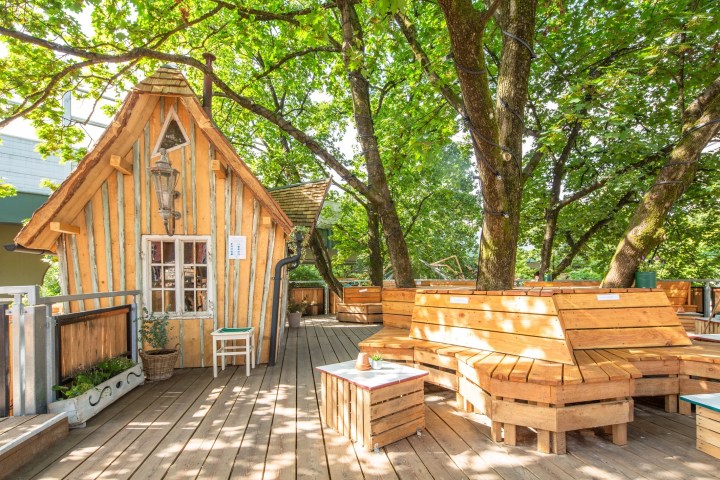 Wooden treehouse with benches on wooden deck under trees.