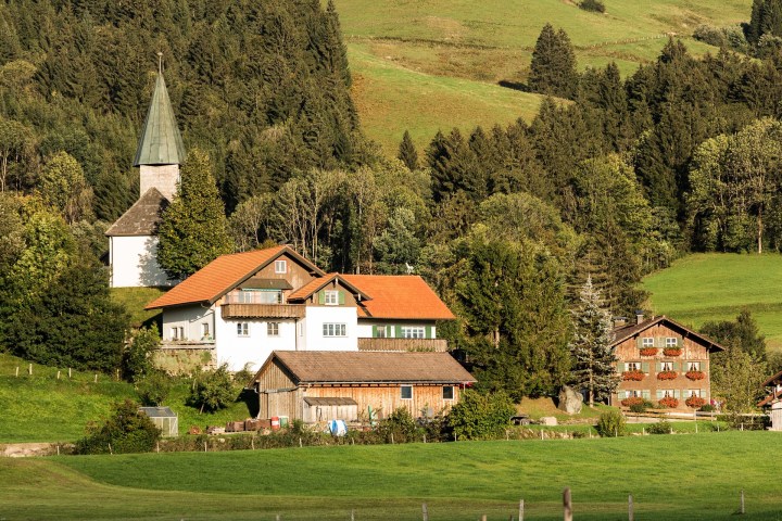 Village houses and church surrounded by trees and lush green hills.