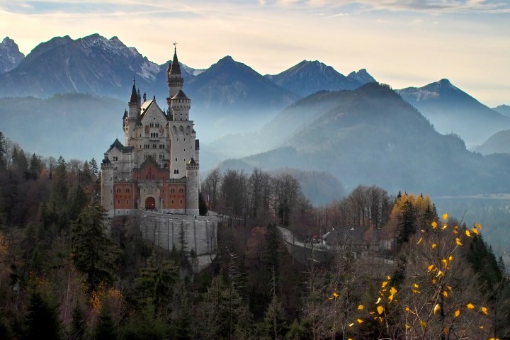Neuschwanstein castle surrounded by misty mountains and trees in autumn colors.