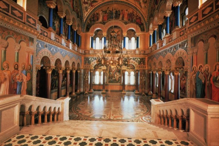 Ornate hall interior with frescoes, arched windows, and chandeliers.