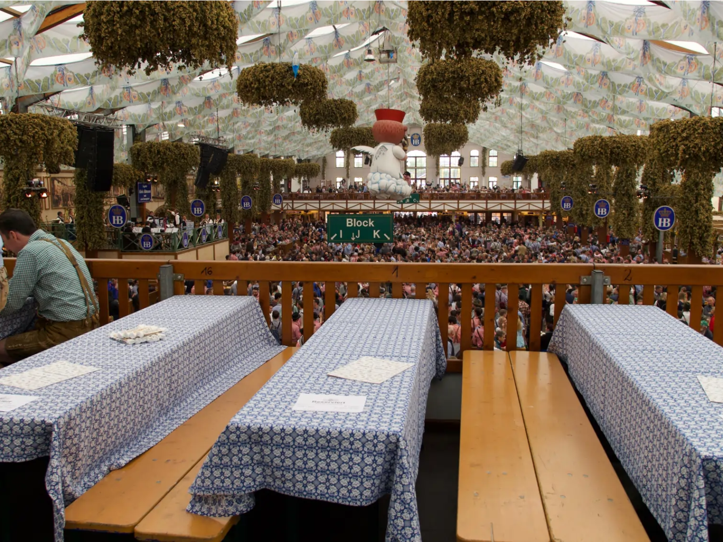 Traditional beer hall with decorated ceiling, hanging hops, and wooden tables during a festival.