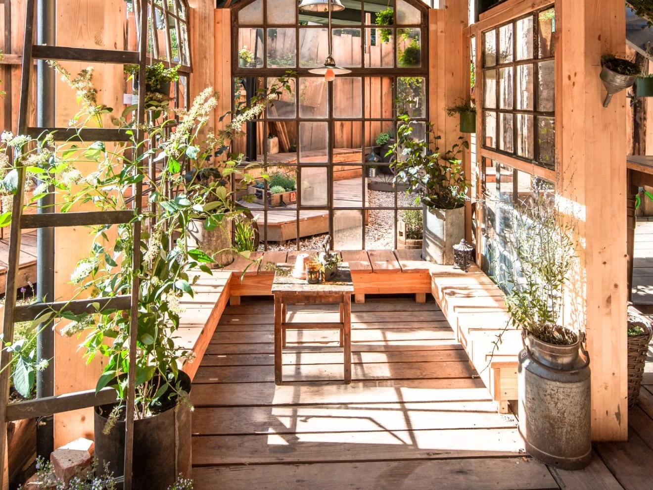 Bright wooden sunroom with large windows, plants, and a small table on a rustic floor.