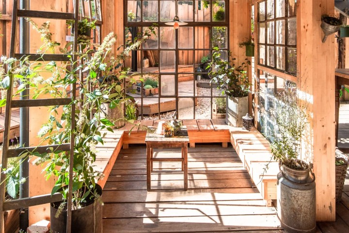 Bright wooden sunroom with large windows, plants, and a small table on a rustic floor.