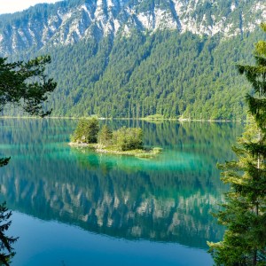 Scenic lake with small island, surrounded by lush green forest and mountains.