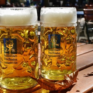Two beer steins on a wooden table with frothy heads and autumn leaves.