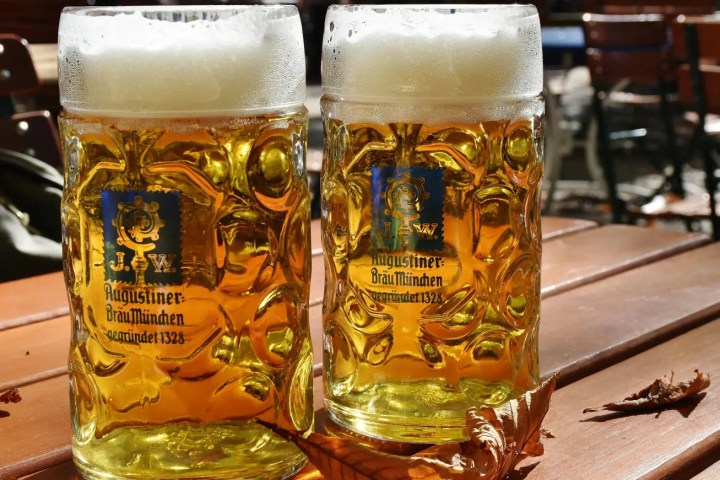 Two beer steins on a wooden table with frothy heads and autumn leaves.