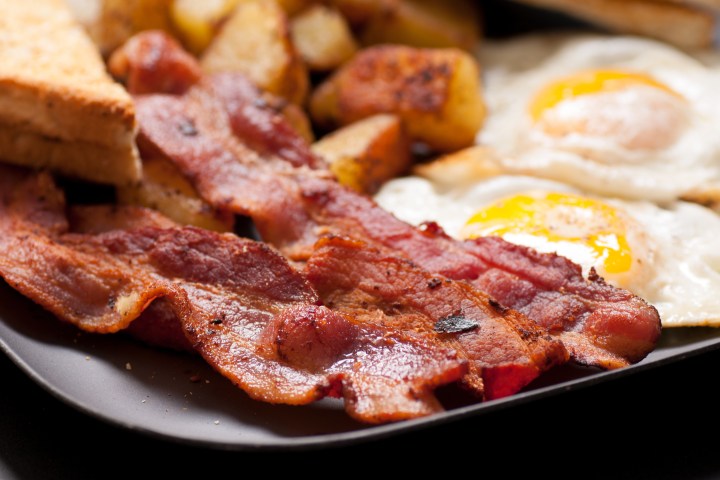 Close-up of breakfast plate with bacon, fried eggs, toast, and potatoes.