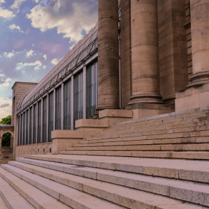 Large stone building with tall columns and steps under a cloudy sky.
