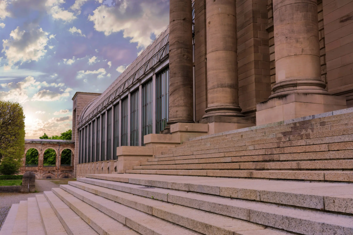 Large stone building with tall columns and steps under a cloudy sky.