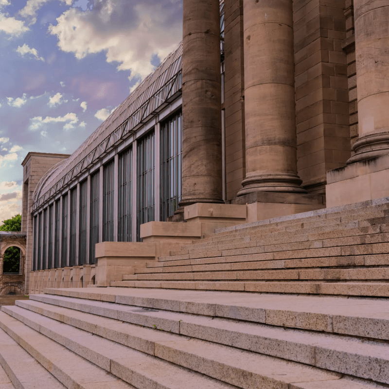 Large stone building with tall columns and steps under a cloudy sky.