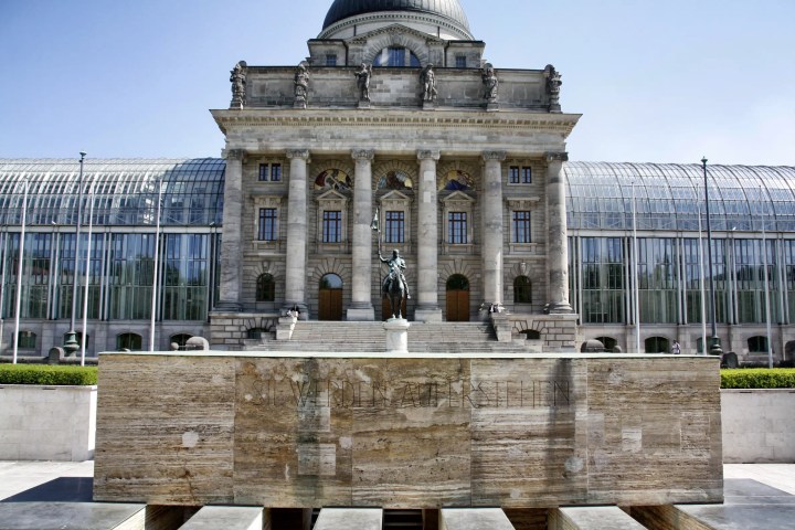 Historic building with columns and a statue in front, featuring glass windows and a dome.