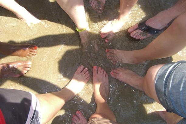 Group of people standing in a circle on wet sand with feet touching water.