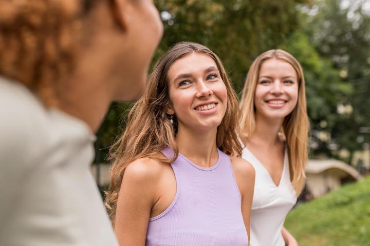 Three women smiling outdoors with trees in the background.