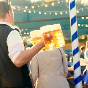 Person carrying beer mugs at an outdoor festival with string lights.