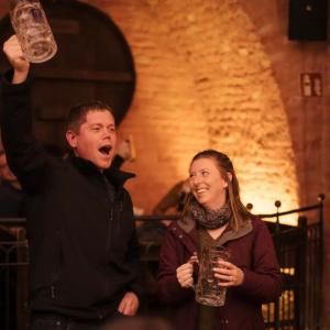 Two people holding empty beer steins, smiling in a brick-walled pub.