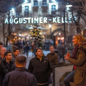 People gathered at a nighttime outdoor event near a building with 'Augustiner-Keller' sign.