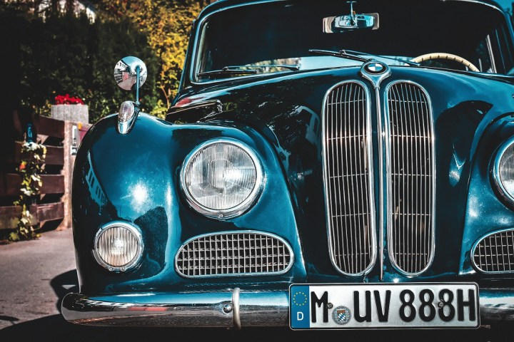 Classic blue car front view with round headlights and a grille, parked on a sunny day.