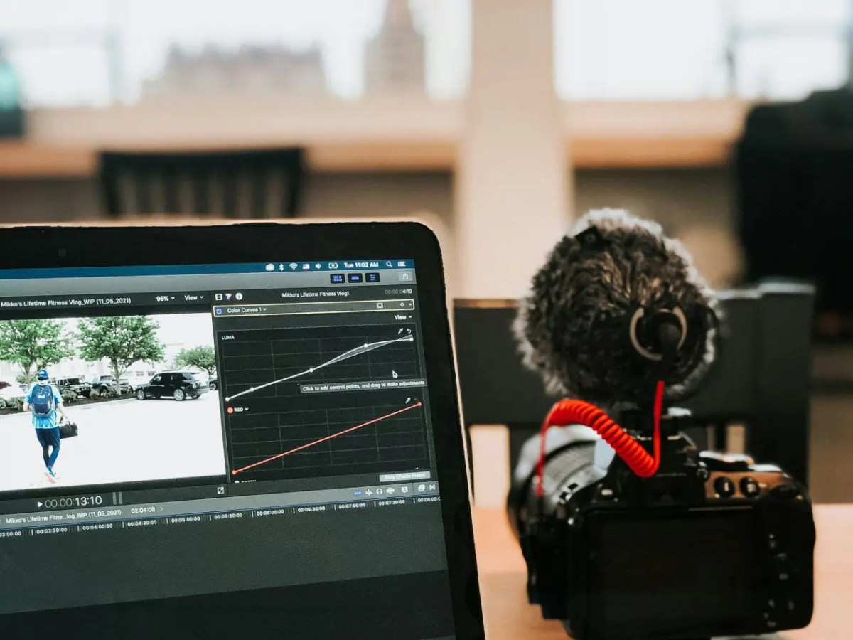 Laptop with video editing software and a camera with a microphone on a desk.