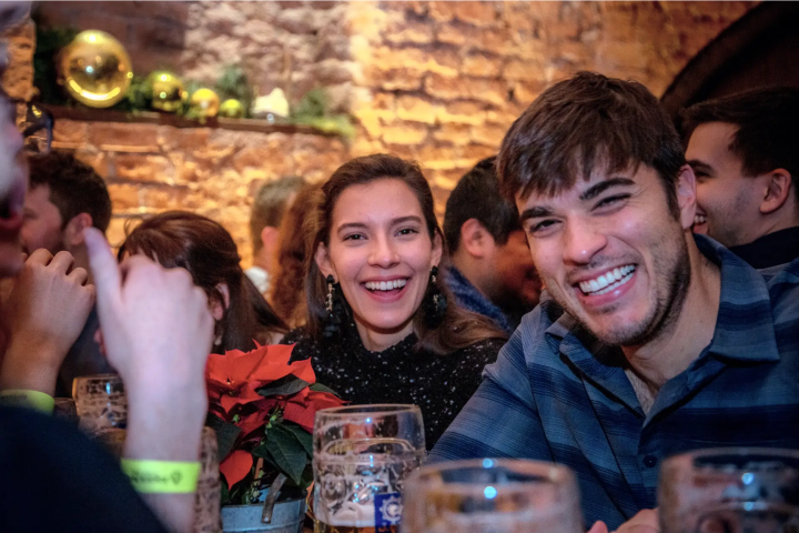 Smiling people in a bar with drinks and holiday decorations on a brick wall.