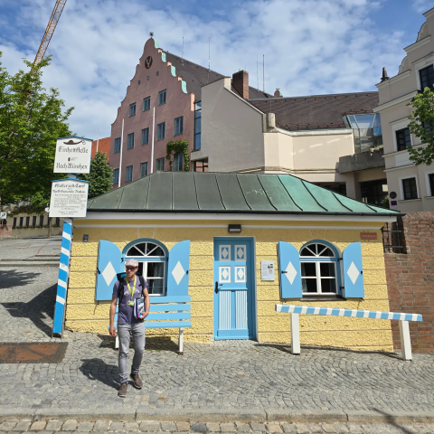 Tour guide with backpack standing near a small yellow building with blue shutters and door. Old cutoms house