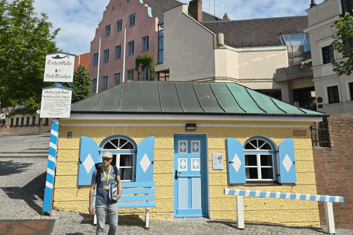 Tour guide with backpack standing near a small yellow building with blue shutters and door. Old cutoms house