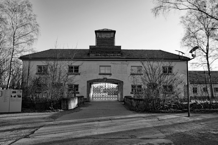Black and white photo of a historical building with an arched gate and trees in the background.