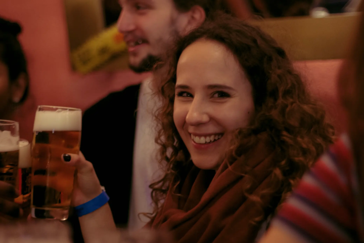 People enjoying drinks at a bar, with a smiling woman holding a beer.