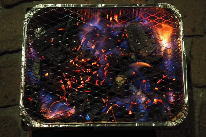 Small portable charcoal grill with glowing coals and flames.