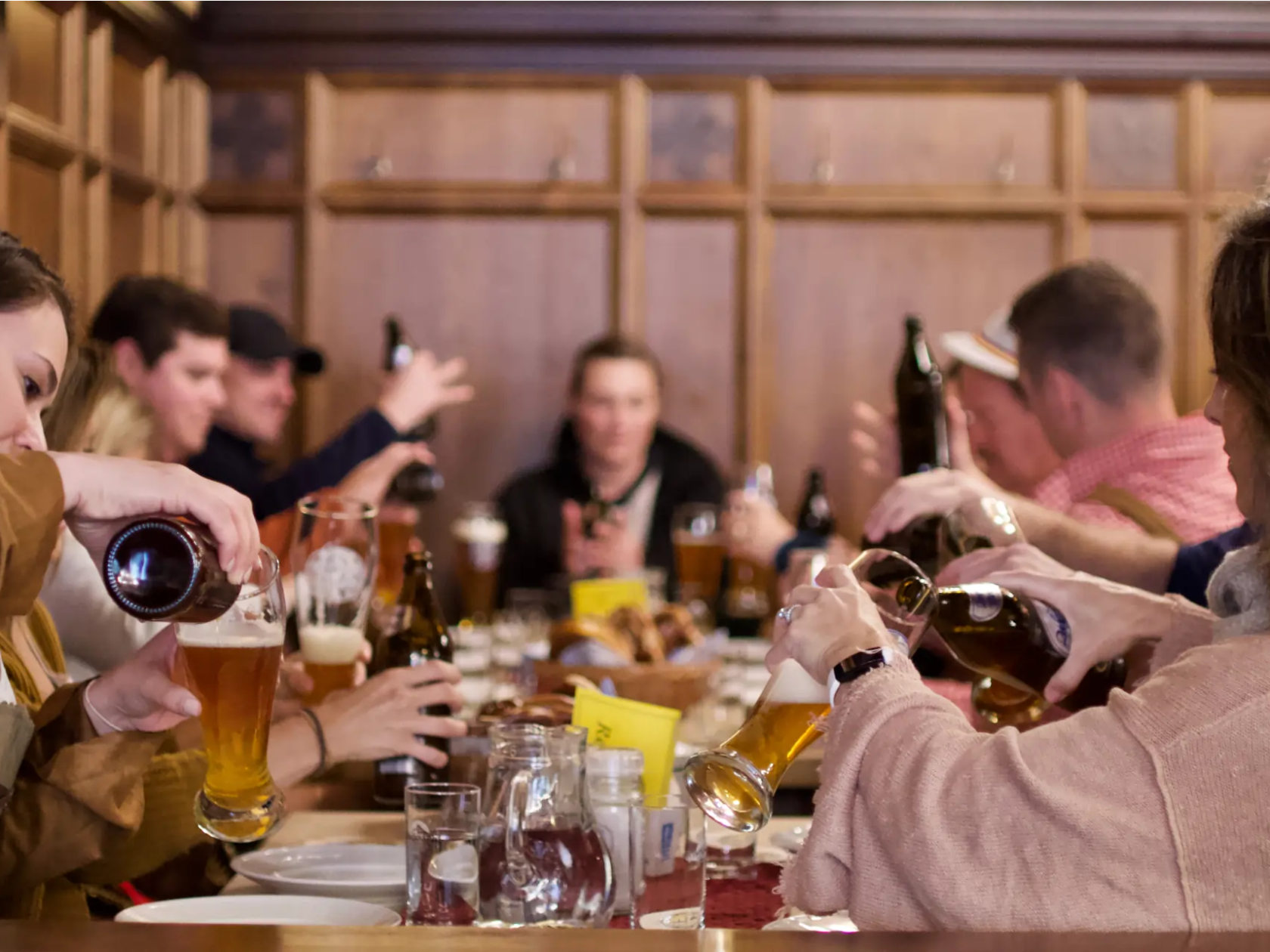 People sitting at a long table, pouring and drinking beer in a cozy wooden room.