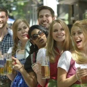 Group of smiling people holding beer mugs in traditional Oktoberfest attire outdoors.