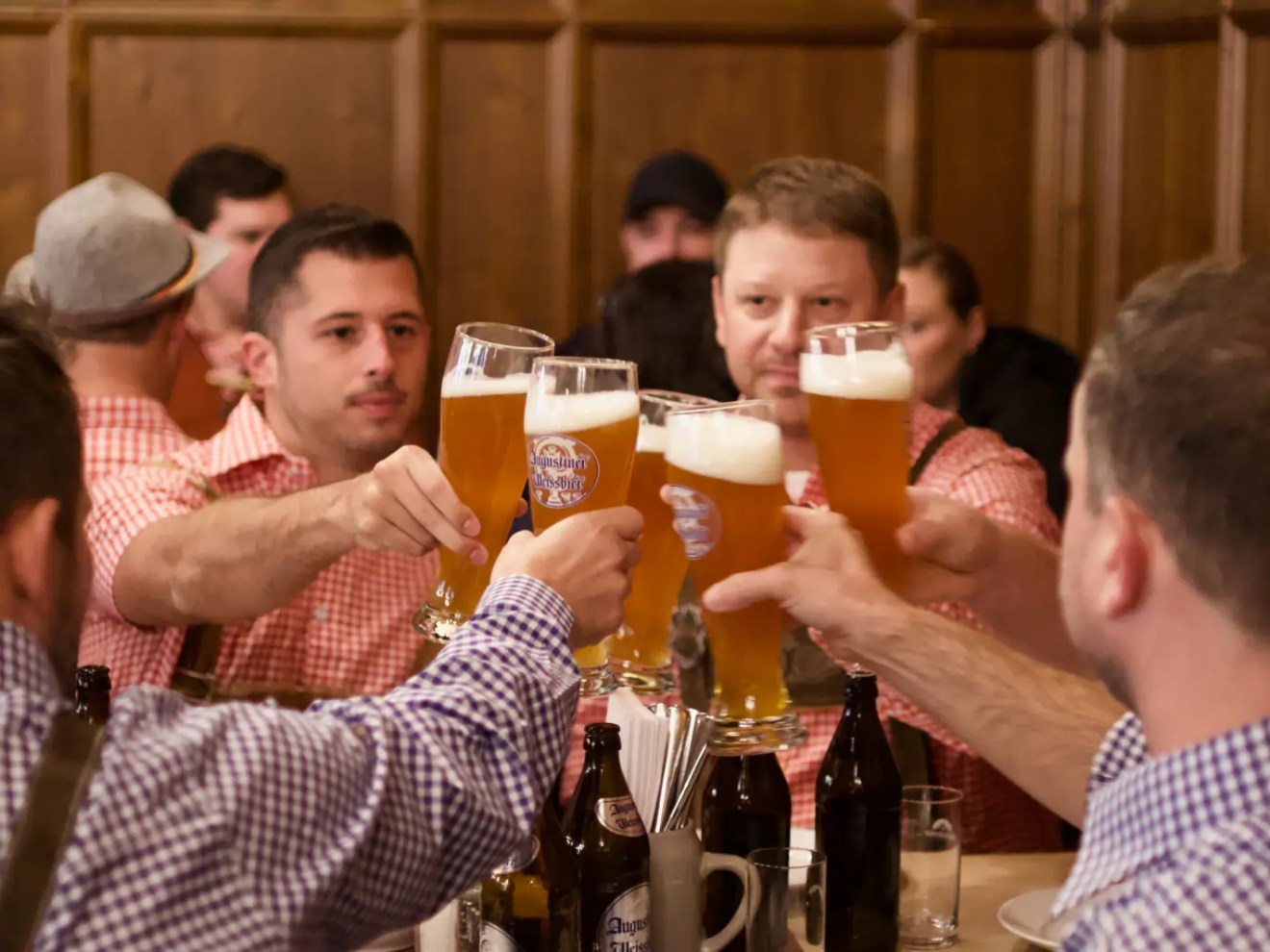 Group of men clinking tall glasses of beer at a wooden table in a pub.