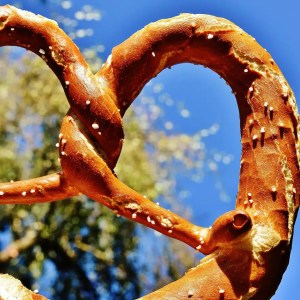 Close-up of a pretzel with salt against a blue sky and blurred tree background.