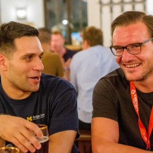 Two men smiling and talking at a table in a crowded bar.