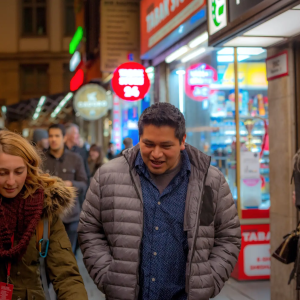 People walking on a street at night with lit-up shop signs and storefronts.