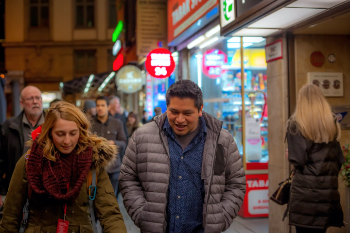 People walking on a street at night with lit-up shop signs and storefronts.