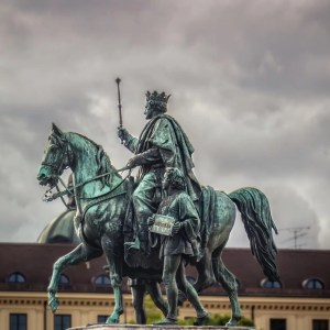 Equestrian statue of a king and squire under a cloudy sky.