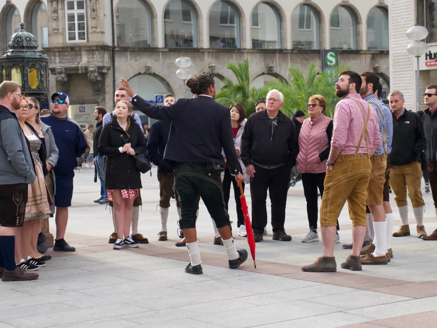 Tour guide with umbrella leads group wearing traditional attire in city square.