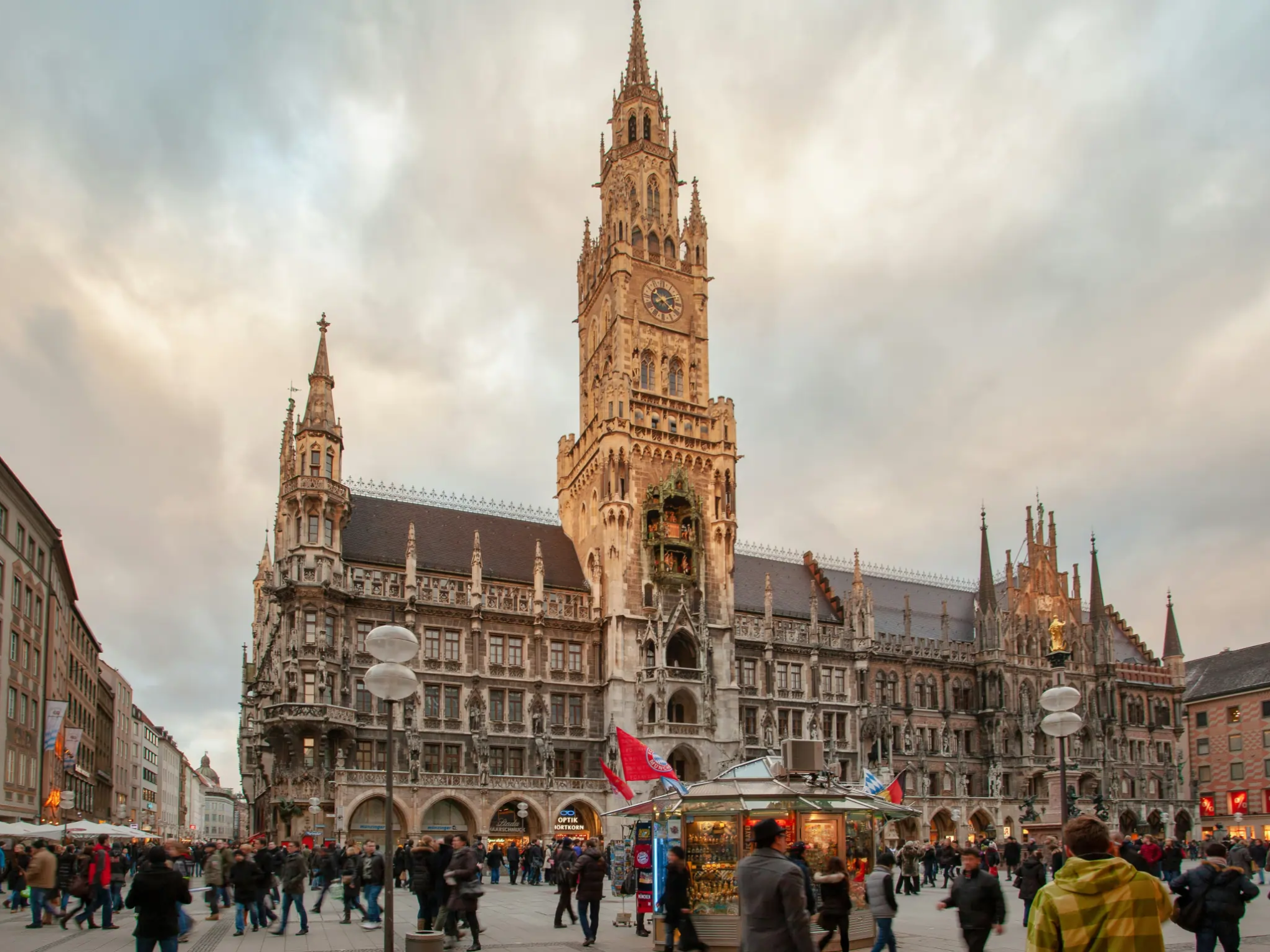 Crowd in front of ornate Gothic building at dusk with cloudy sky.