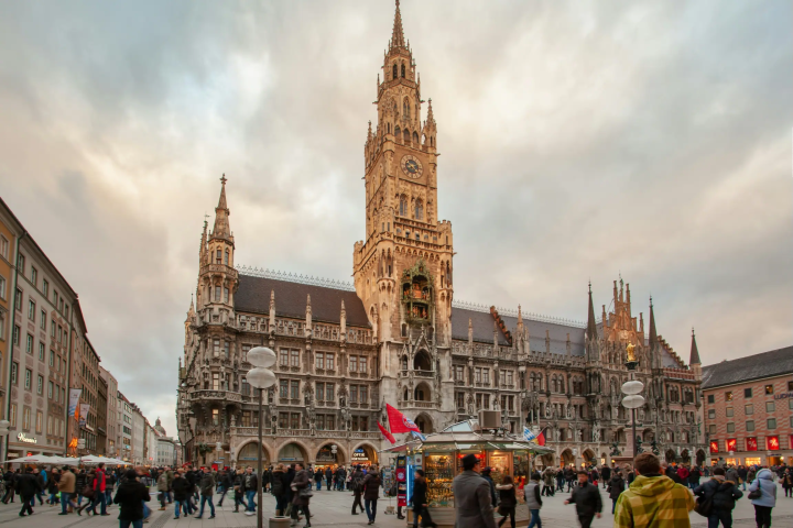 Crowd in front of ornate Gothic building at dusk with cloudy sky.