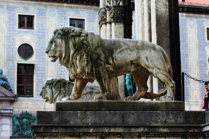 Stone lion statues in front of a historic building with arched windows and decorative columns.