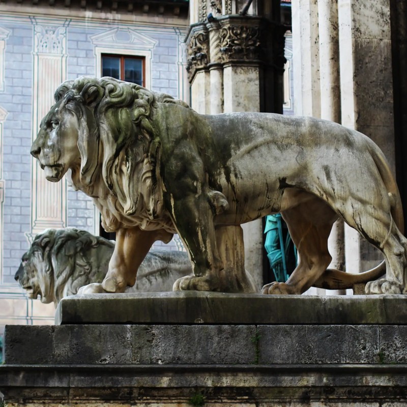Stone lion statues in front of a historic building with arched windows and decorative columns.